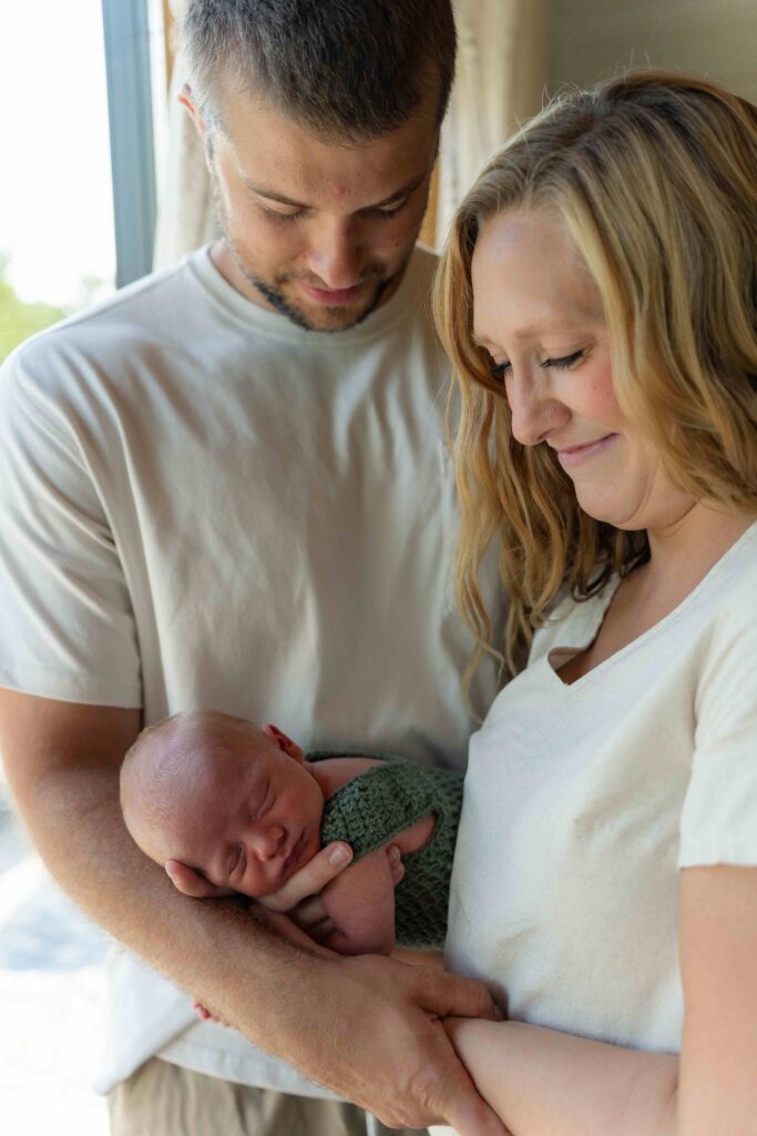 Mom and dad hold their 3rd newborn son in their home in Boone North Carolina during an in-home lifestyle family newborn session.