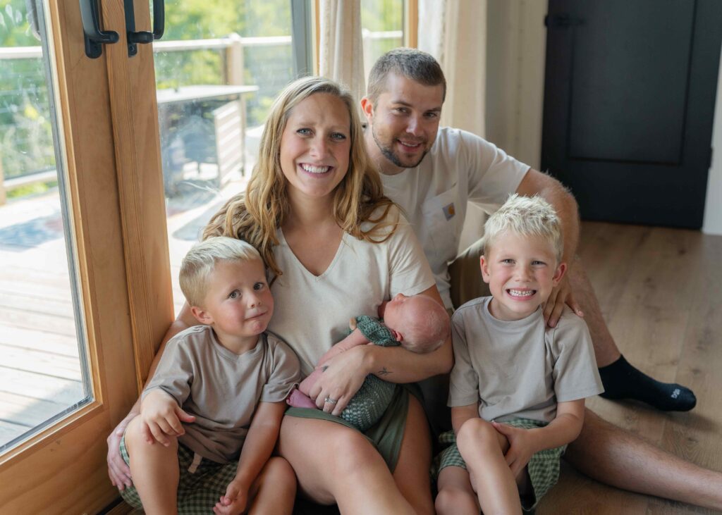 Family of five sits on the floor of their home in Boone North Carolina during a lifestyle newborn session to get a family photograph.