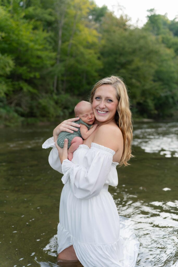 Mother holds newborn baby against her face while standing in the river of her property in Boone North Carolina during a lifestyle maternity session.